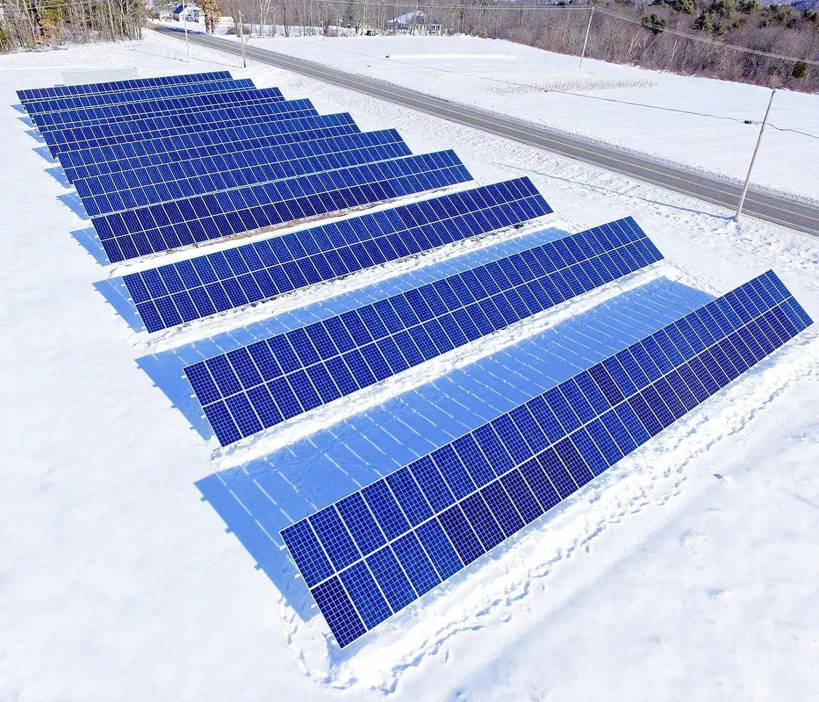Rows of solar panels stand in a snow-covered community solar field.