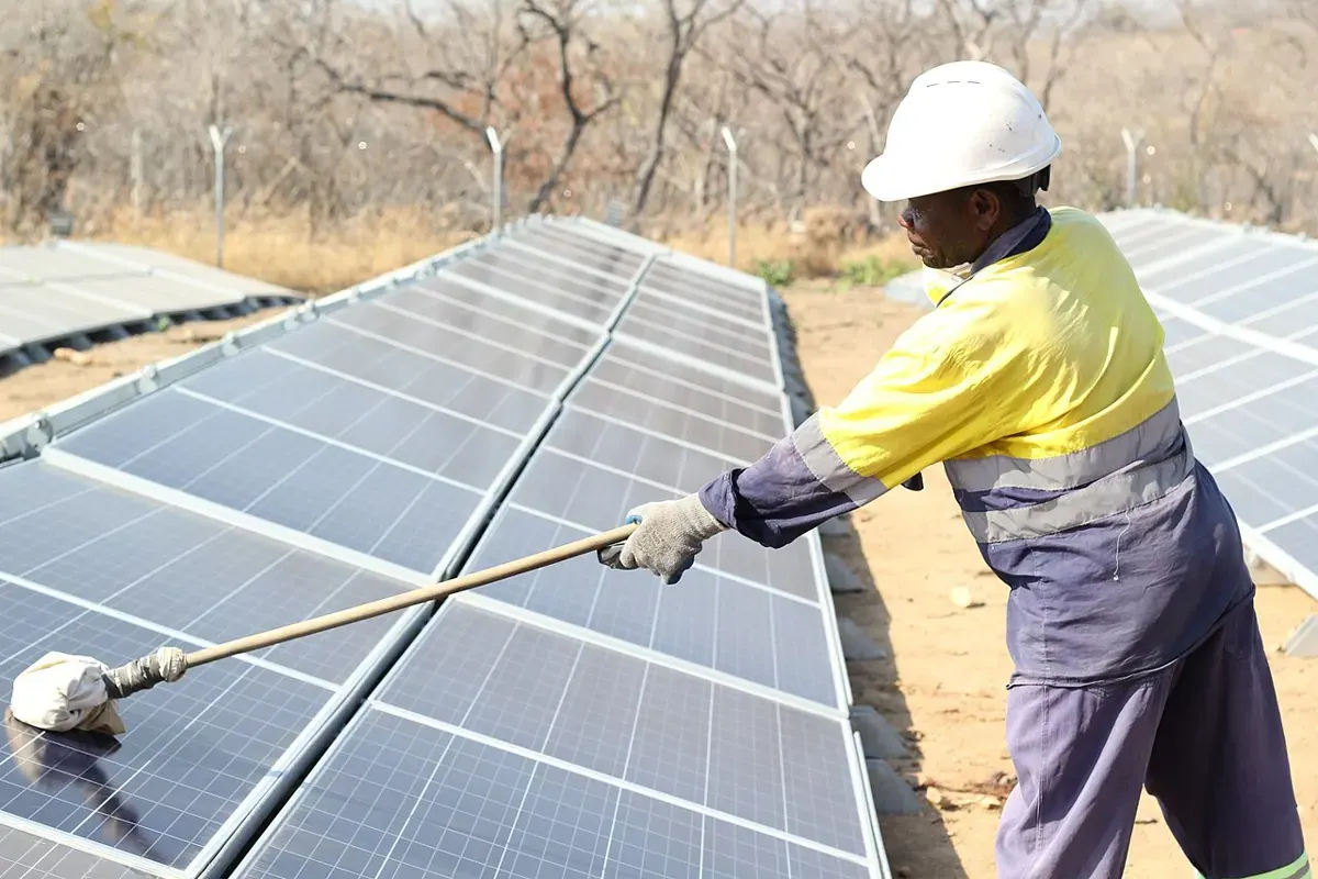 A technician cleans solar panels with a long-handled tool.