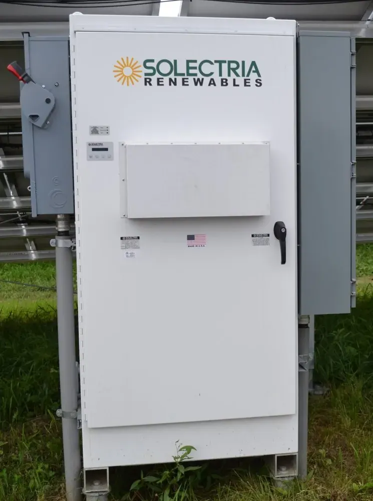 An outdoor solar inverter cabinet beside a photovoltaic installation.