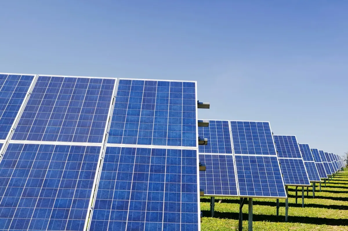 Blue photovoltaic panels arranged in a field beneath a clear sky.