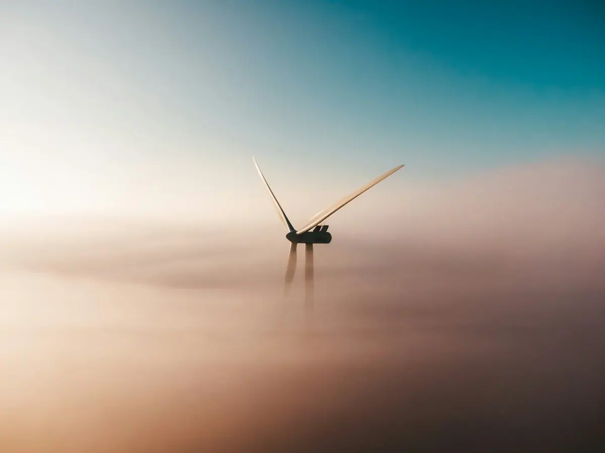 A wind turbine emerges above mist in soft evening light.