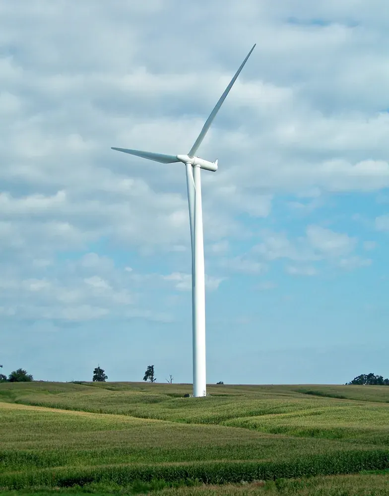 A wind turbine in an open agricultural landscape beneath scattered clouds.