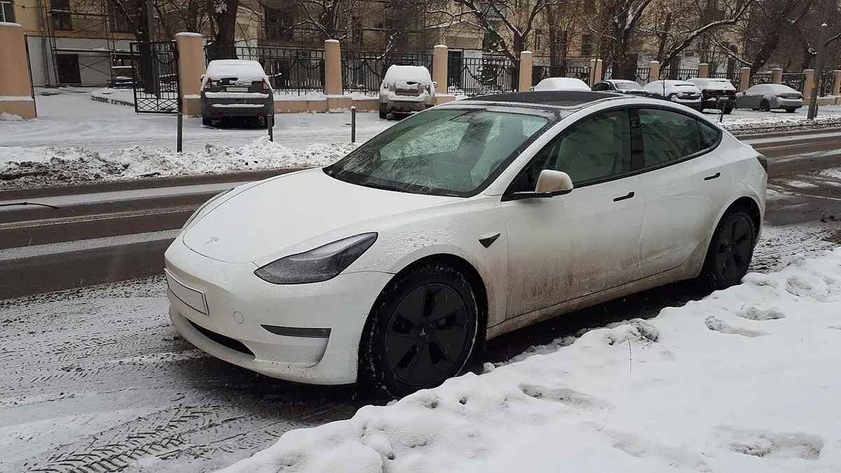 A white Tesla electric car parked on a snowy street.