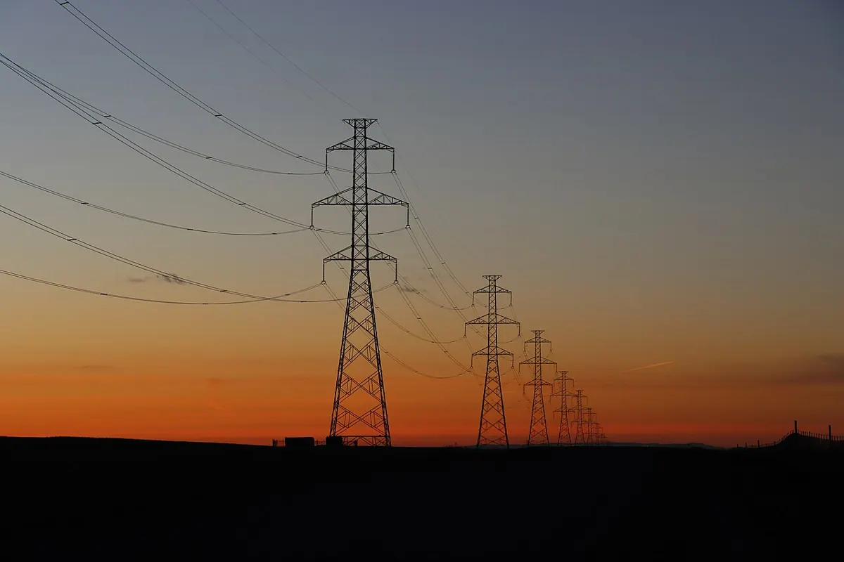 Electricity transmission towers silhouetted against a sunset sky.