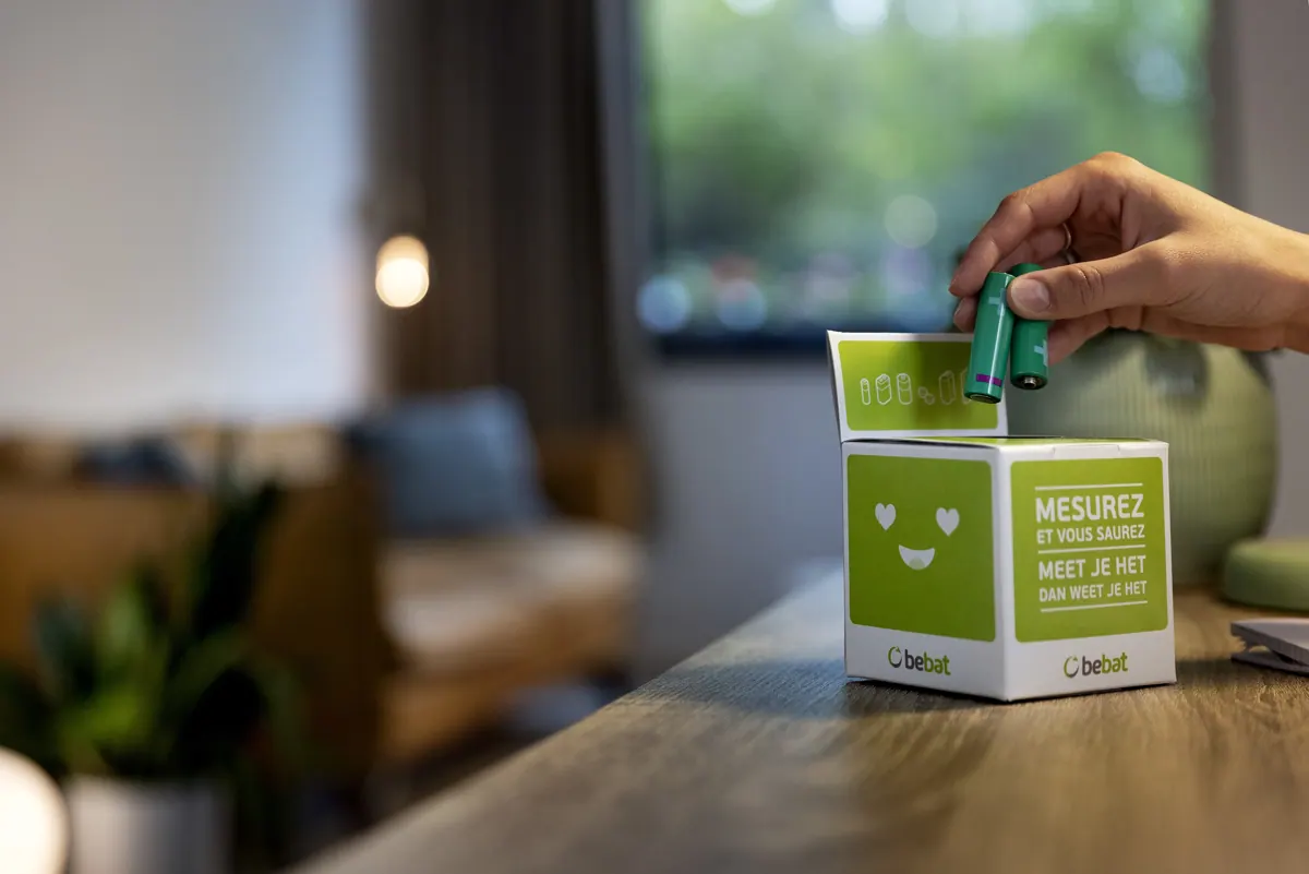 A hand places a used battery into a household collection box.