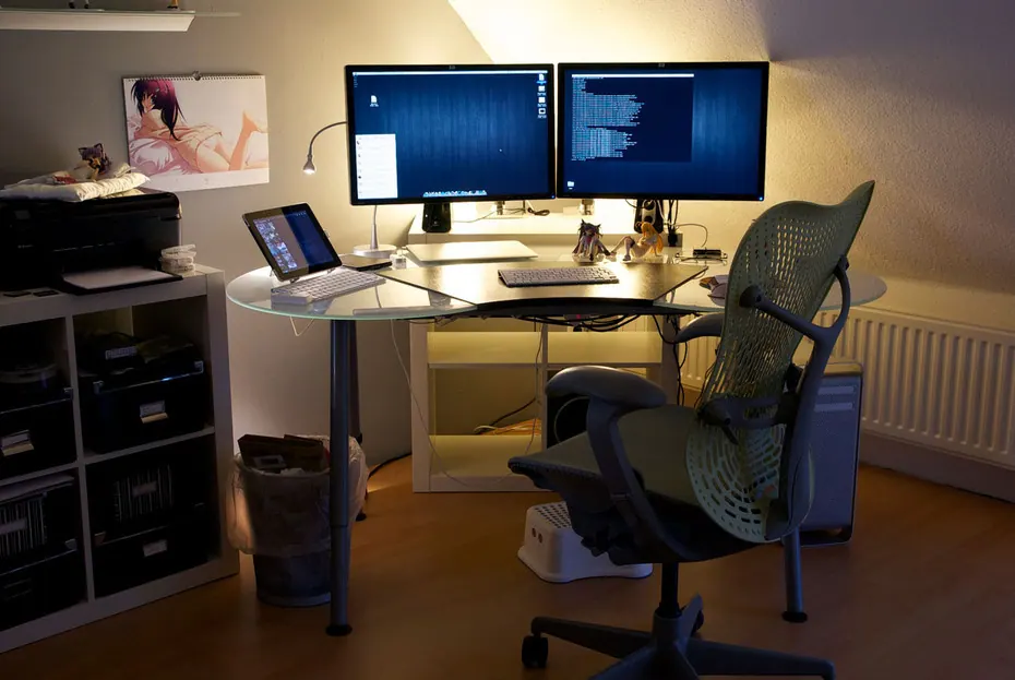 A home office desk holds computer screens and everyday work equipment.